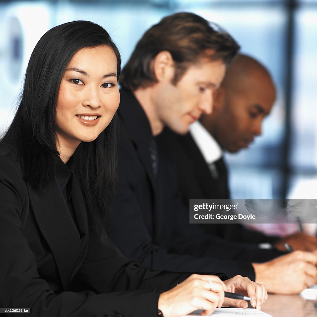 Portrait of a young businesswoman and two businessmen sitting at a meeting (blurred)