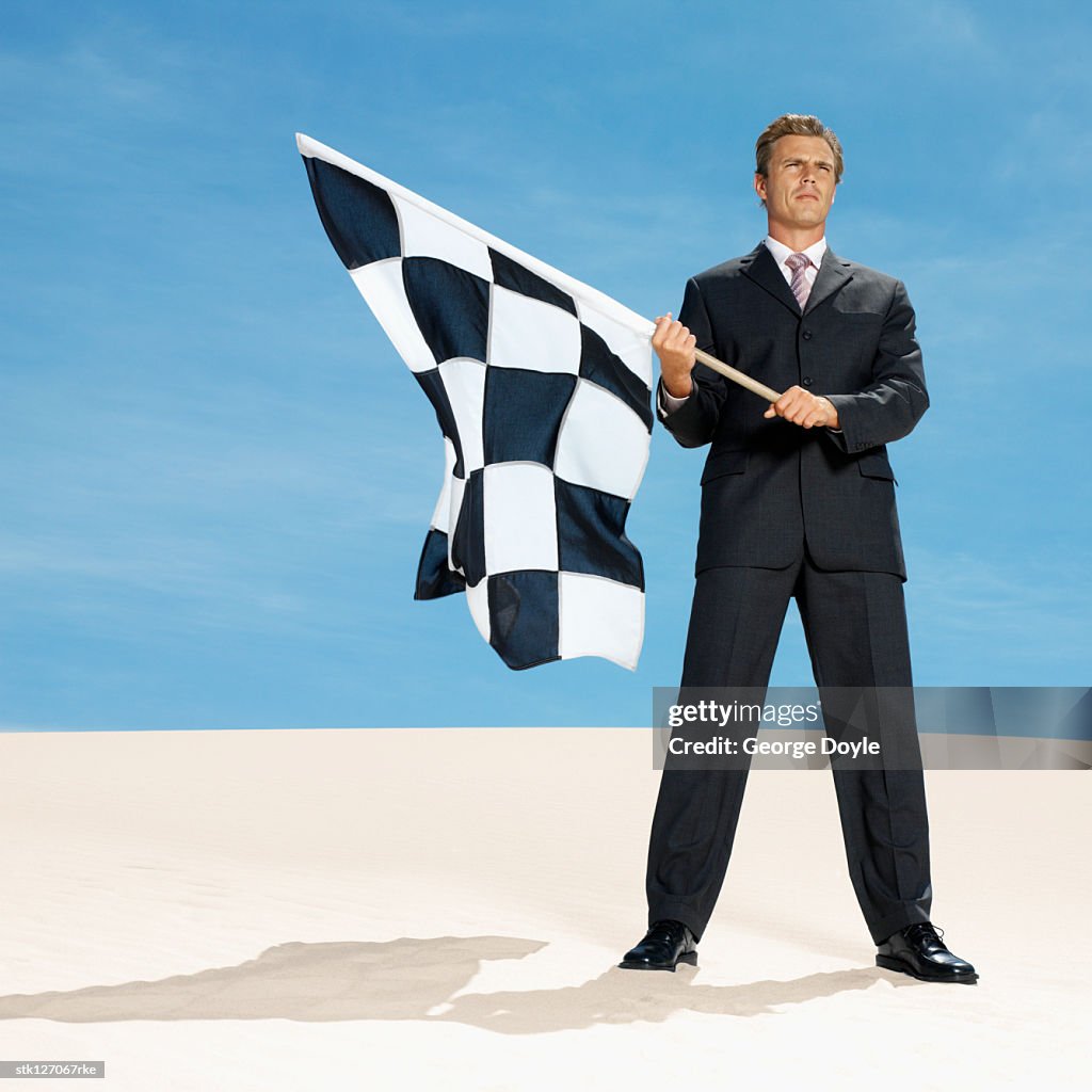 Businessman in desert waving chequered flag, low angle view