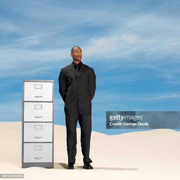 young man standing next to a file cabinet in the desert - file cabinet stock-fotos und bilder