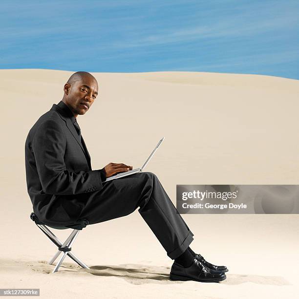 side profile of a young man sitting on a chair operating a laptop - laptop desert stock pictures, royalty-free photos & images