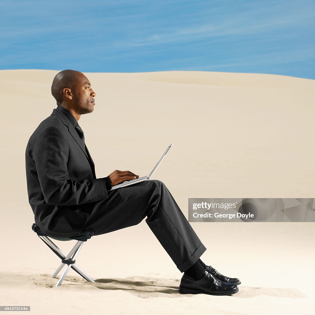 Businessman in desert working on laptop computer, side view