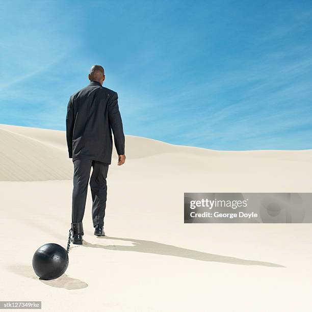 businessman wearing ball and chain in desert rear view, low angle view - restraining device stock pictures, royalty-free photos & images