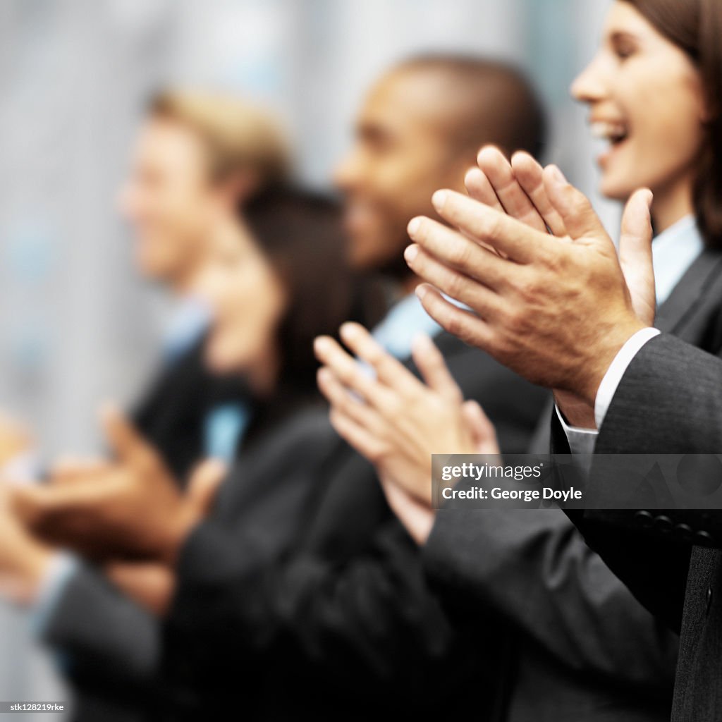 Side profile of a group of young executives clapping (blurred)