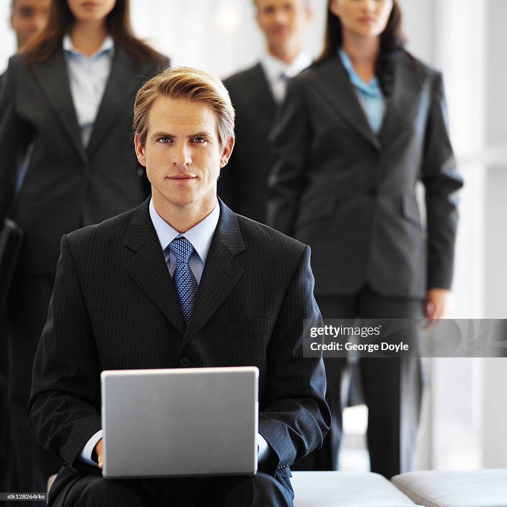 Young businessman working on a laptop with executives standing behind