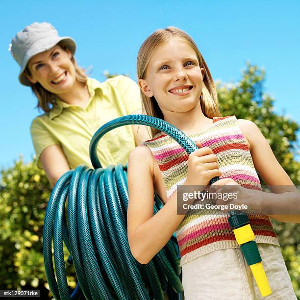 portrait of a mother and daughter holding a garden hose in the yard - george nader stockfoto's en -beelden