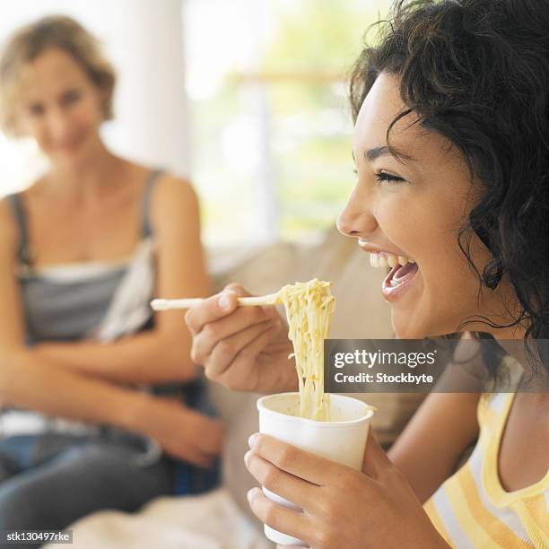 portrait of a young woman smiling and eating noodles from a cup - cup noodles stock-fotos und bilder