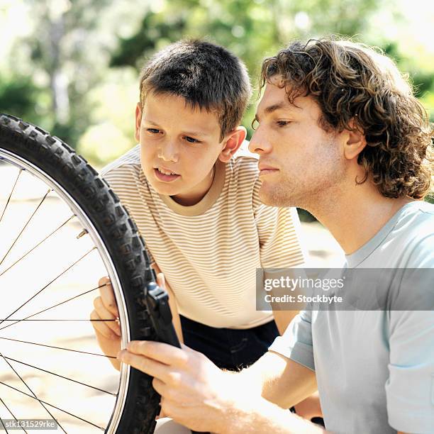 close up of father and son (8-9) pumping tyre of bicycle in countryside - genderblend stock-fotos und bilder
