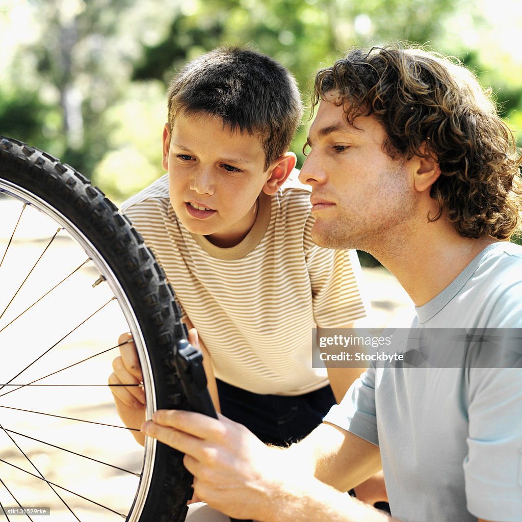 Close up of father and son (8-9) pumping tyre of bicycle in countryside