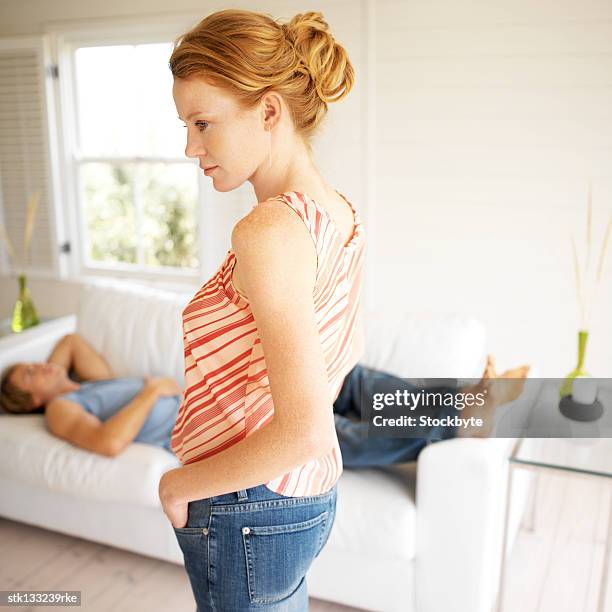 side profile of a woman standing in a living room with a man sleeping on the couch - living stock-fotos und bilder