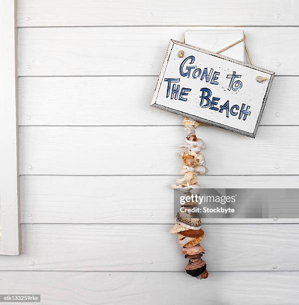 close-up of a signboard hung on a wall with a string of shells hanging under it - string - fotografias e filmes do acervo