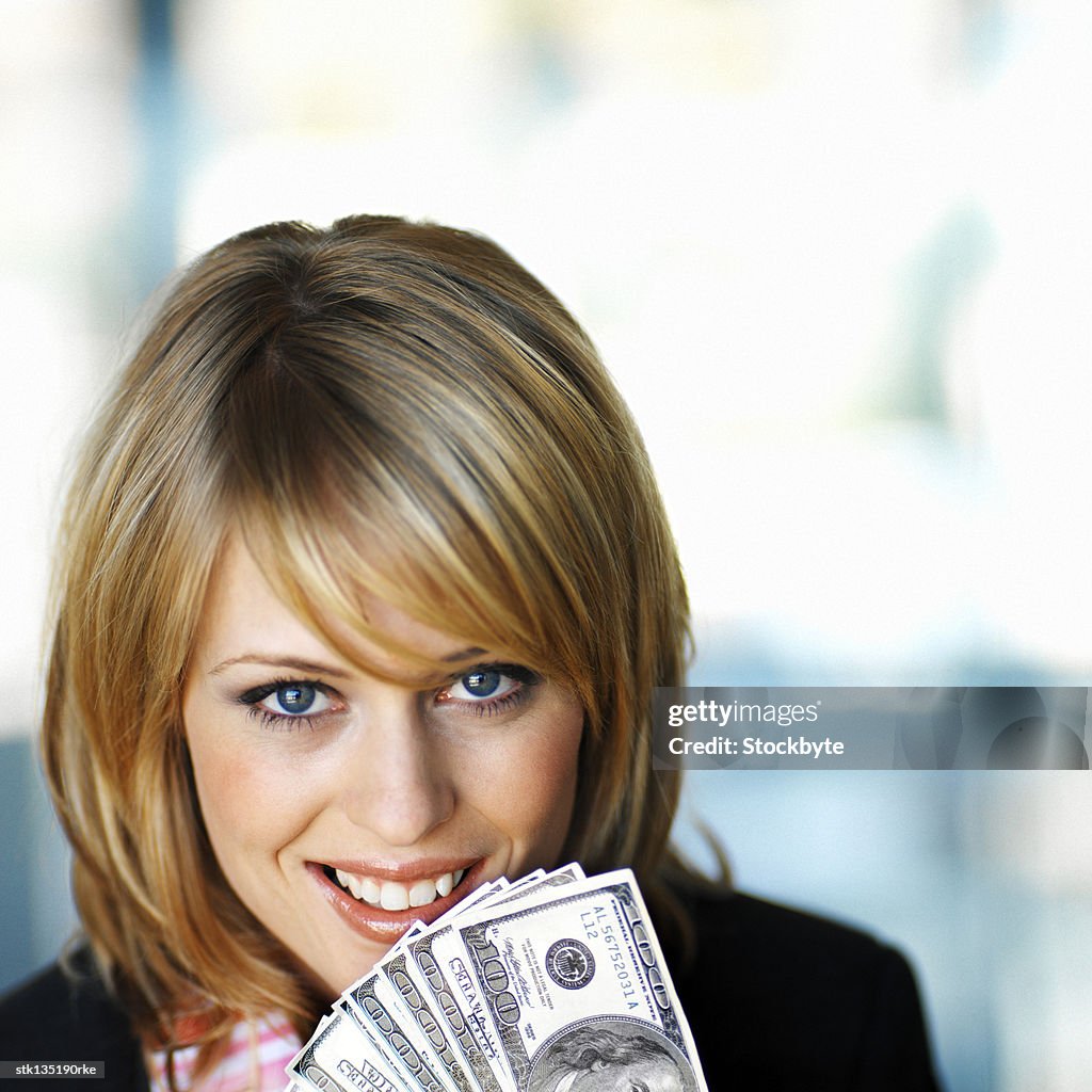 Close-up of a woman holding hundred dollar bills to her face