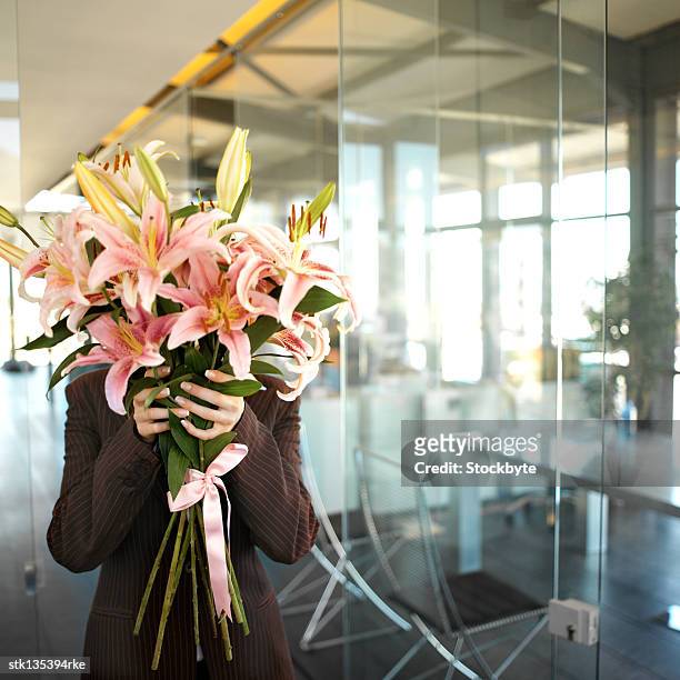 businesswoman holding a bunch of flowers to cover her face - lily family photos et images de collection