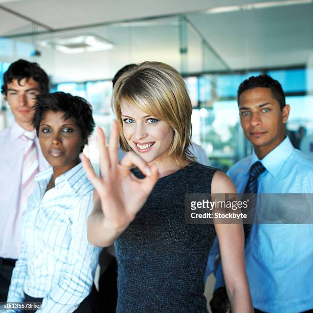 portrait of a young businesswoman giving the ok hand signal with young business executives standing behind - signal stock-fotos und bilder