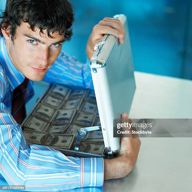 portrait of a businessman holding an open briefcase full of money - yuppie stock-fotos und bilder