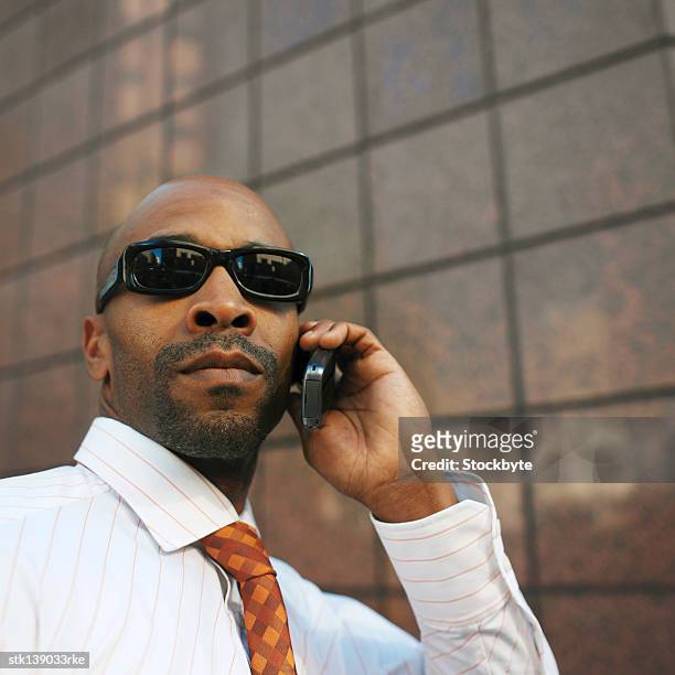 close-up of a businessman wearing sun glasses talking on a mobile phone - best sunglasses for bald men fotografías e imágenes de stock