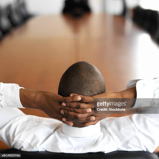 business man relaxing with his hands on his head in an empty conference room (blurred) - stretching hands behind head rear view stock-fotos und bilder