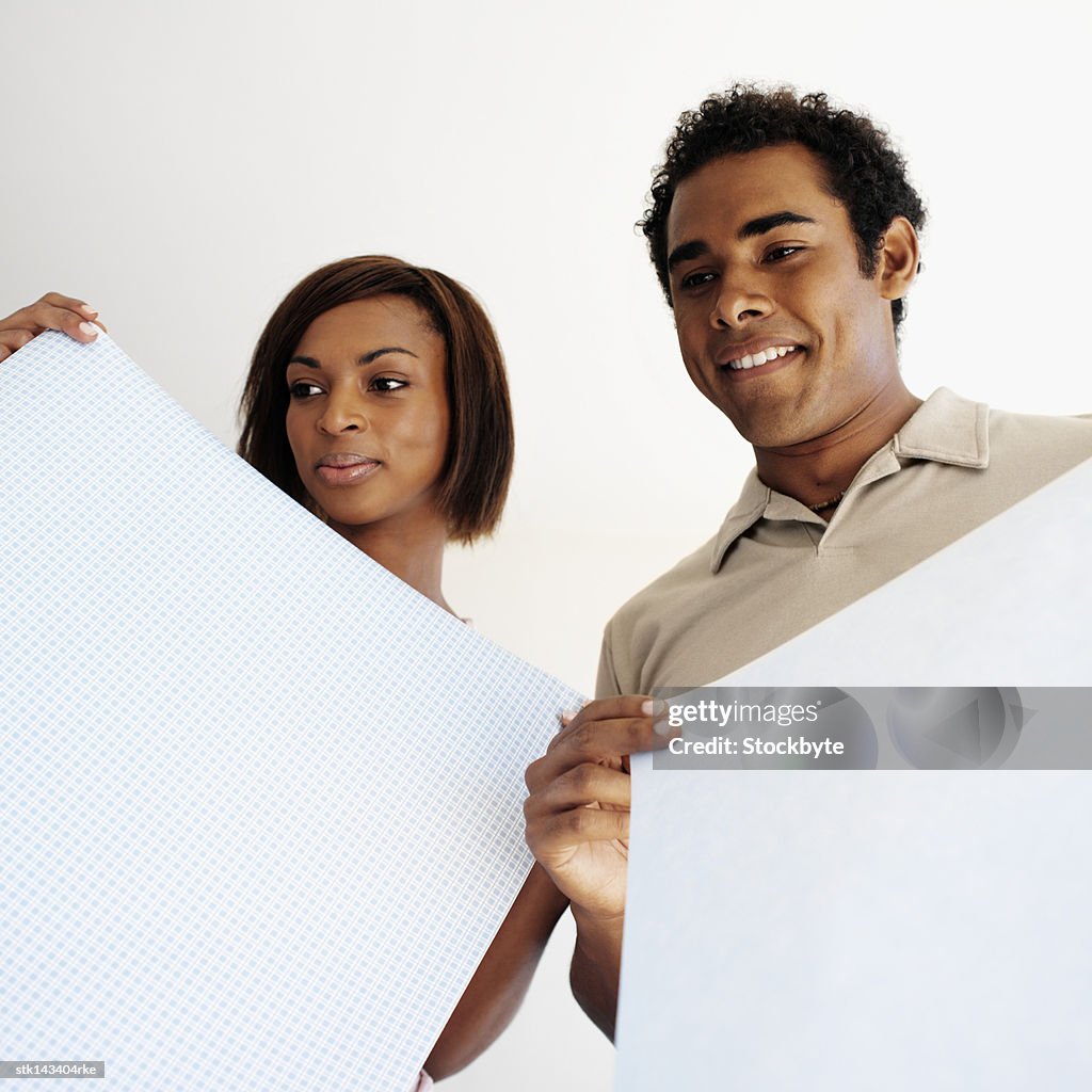 Low angle view of a couple holding up white wallpaper