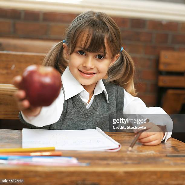 portrait of a young girl at school holding out an apple - teachers pet stock pictures, royalty-free photos & images