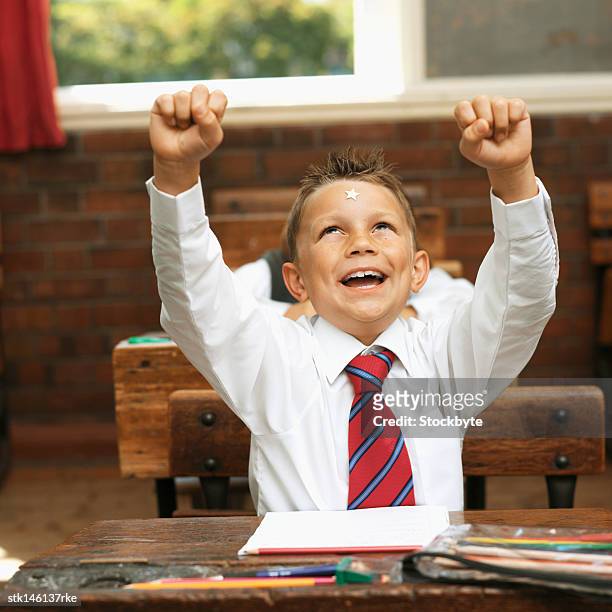 boy (9-11) in a classroom raising his arms with a star on his forehead - stars of formula one and music make a noise at abbey road studios to help children locked away in orphanages stockfoto's en -beelden