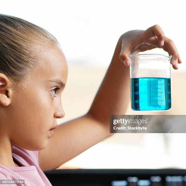 side profile of a little girl holding up a beaker holding a blue liquid - kittle stock-fotos und bilder