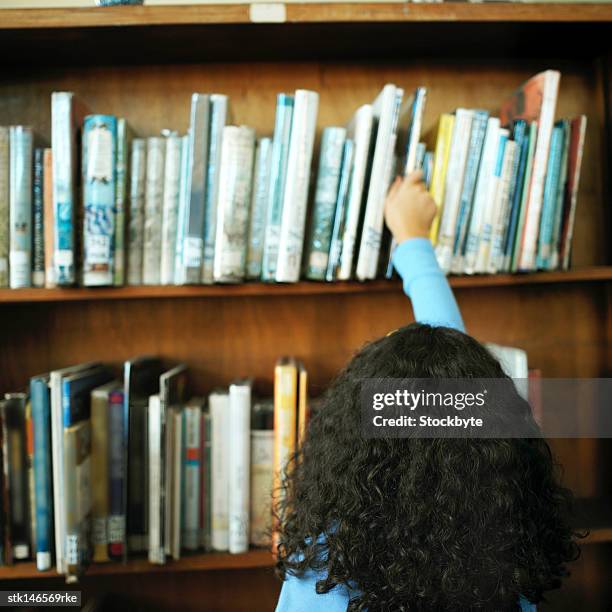 rear view of a girl (10-12) taking a book from a library shelf - middle childhood stock pictures, royalty-free photos & images
