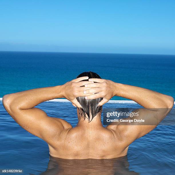 young man in swimming pool with his hands on his head rear view - stretching hands behind head rear view stock-fotos und bilder