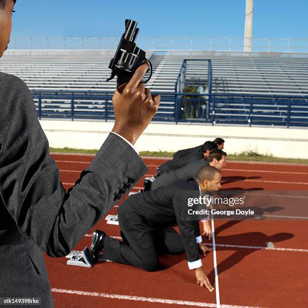 person holding a starters pistol and businessmen at starting positions on a running track - startschot stockfoto's en -beelden