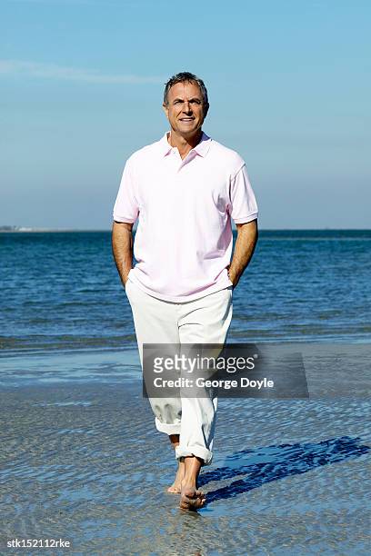 elderly man smiling walking on the beach with his hands in his pockets - men's water polo stockfoto's en -beelden