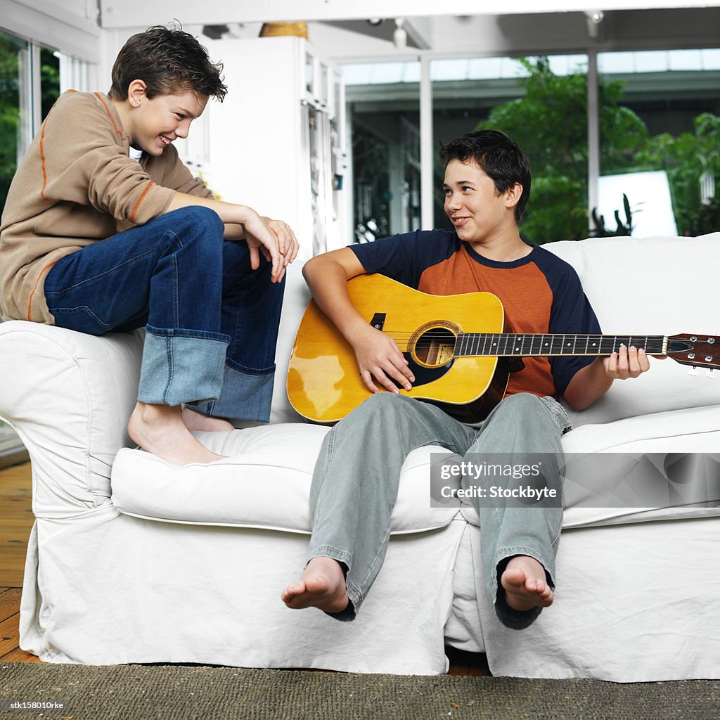 Two brothers laughing and playing guitar sitting on a sofa