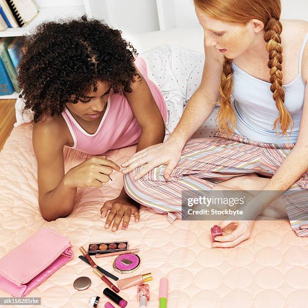 two young girls sitting on bed with cosmetics and applying nail polish - night in fotografías e imágenes de stock