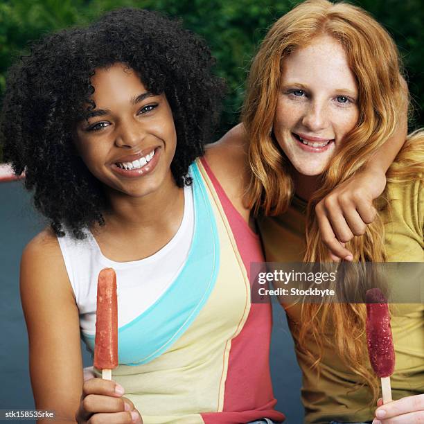 portrait of two young girls eating ice lollies smiling - gefrorene süßspeise stock-fotos und bilder