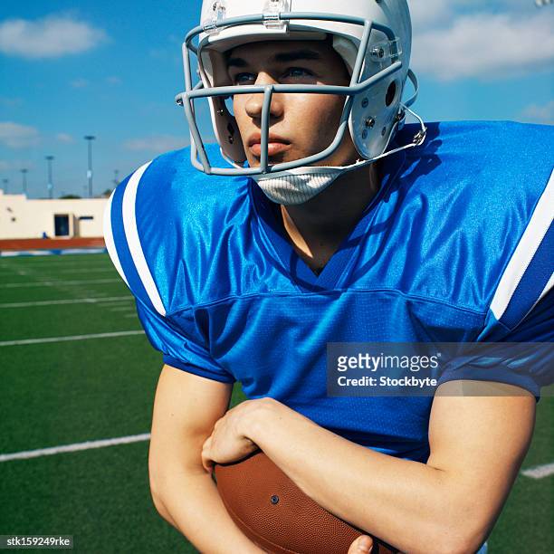 american football player (16-20) holding football looking into the distance - football player imagens e fotografias de stock