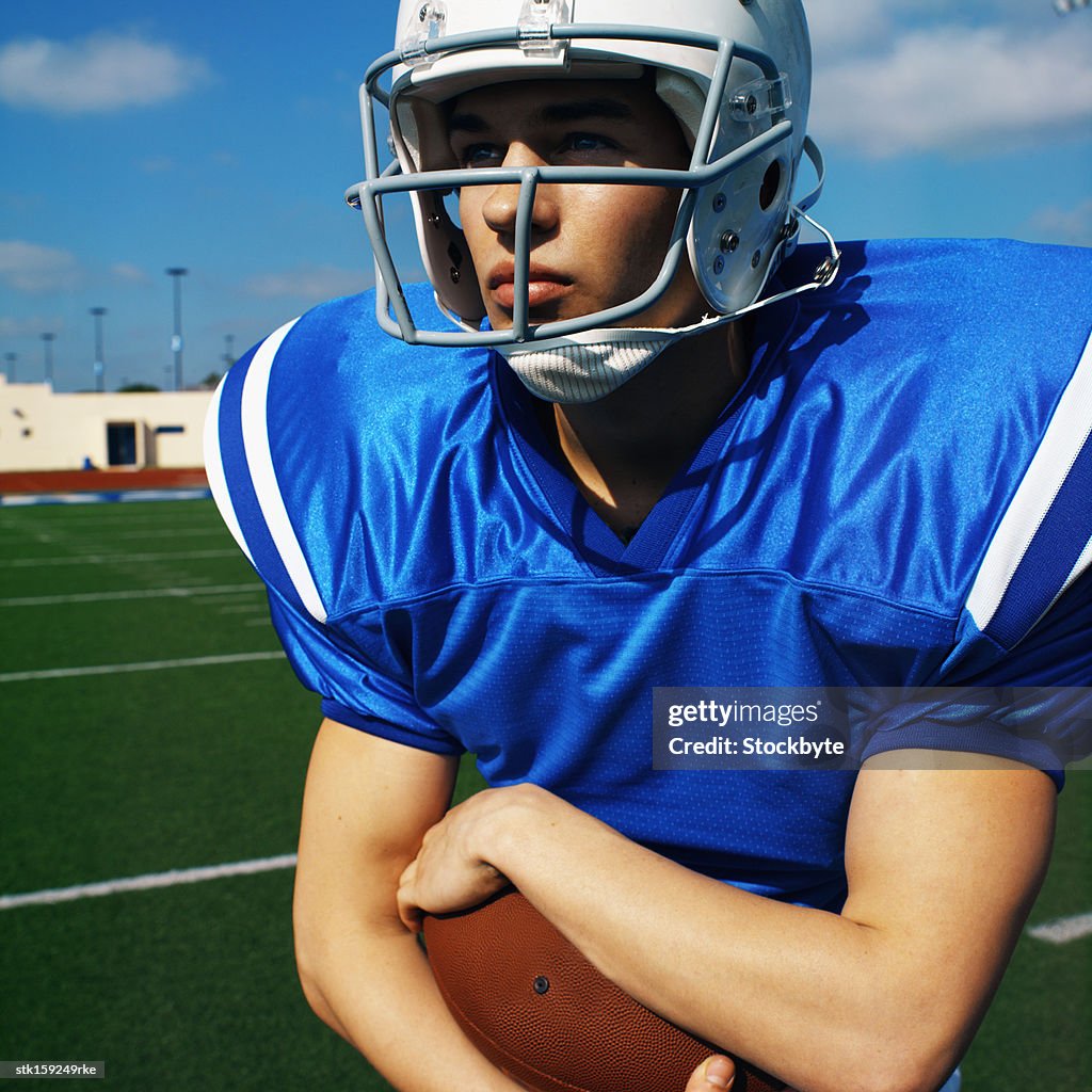 American football player (16-20) holding football looking into the distance