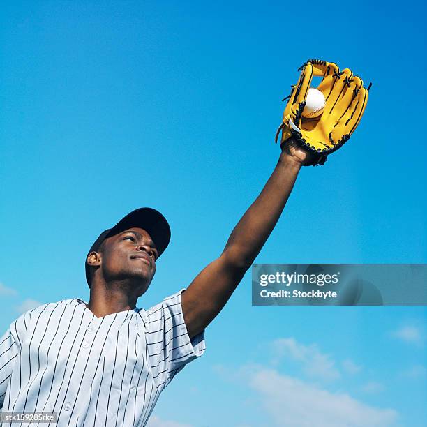 low angle view of a baseball player wearing a baseball mitt catching a ball - vangershandschoen stockfoto's en -beelden