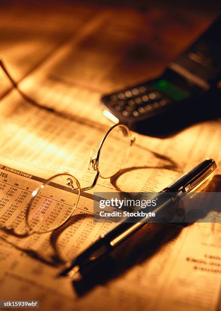 close-up of spectacles and a pen lying with a mobile phone - share prices of consumer companies pushes dow jones industrials average sharply higher stockfoto's en -beelden