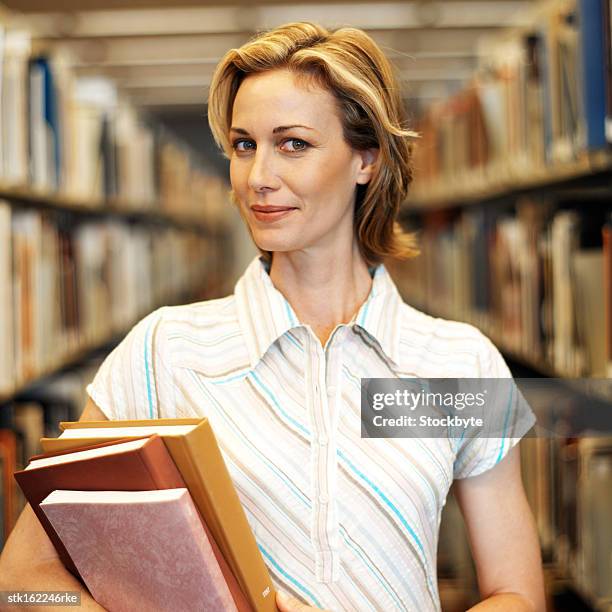 portrait of a young woman standing between two shelves of files holding books - between stock-fotos und bilder