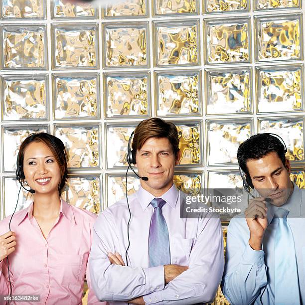 three businesspeople wearing telephone headsets standing against glass wall portrait - informational stock pictures, royalty-free photos & images