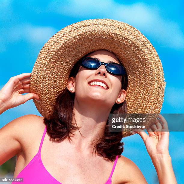 low angle view of a young woman wearing a straw hat smiling - hat stock-fotos und bilder