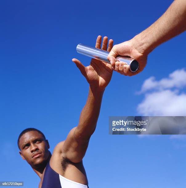 low angle view of two young male athletes exchanging the baton in a baton relay race - baton relay bildbanksfoton och bilder
