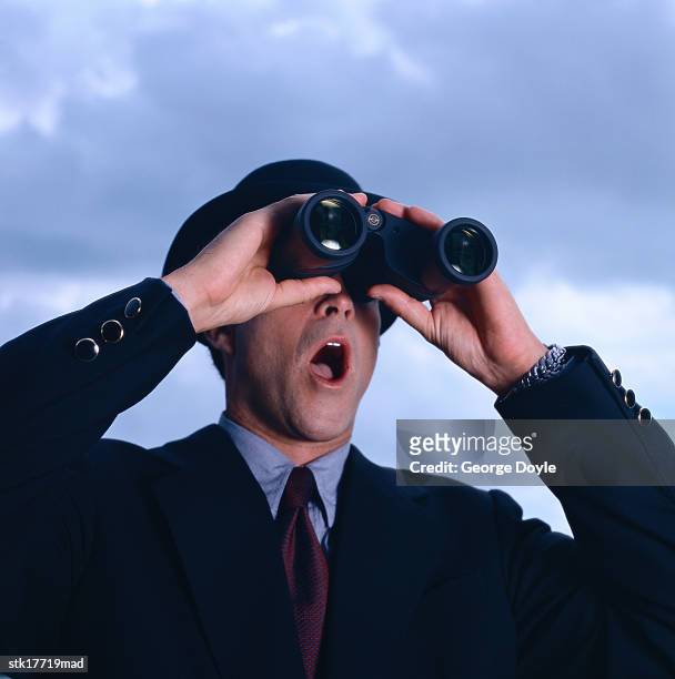 close-up of a businessman in a hat looking through binoculars with mouth open - hat stock-fotos und bilder