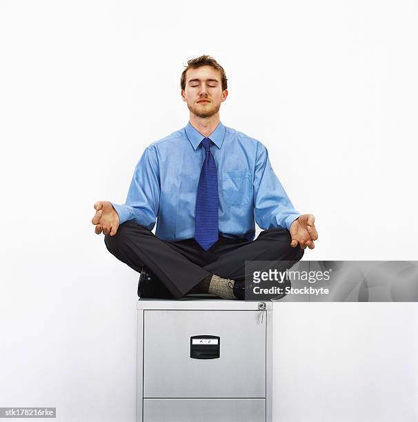 portrait of a young man sitting on top of a file cabinet meditating - file cabinet stock-fotos und bilder