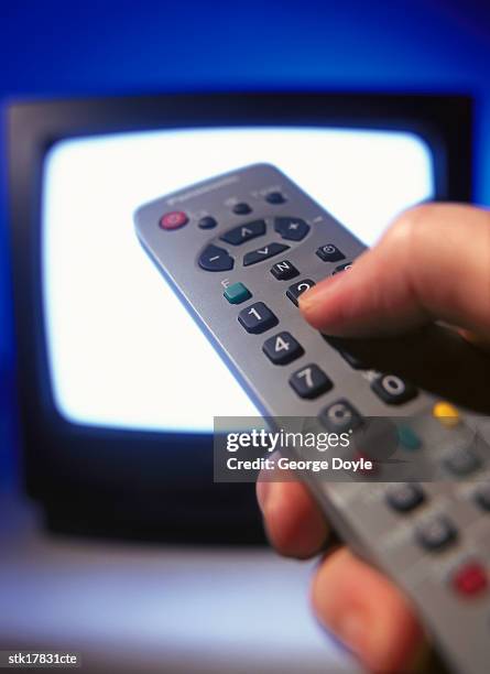 close-up of a hand operating a remote control pointed towards a television - control photos et images de collection