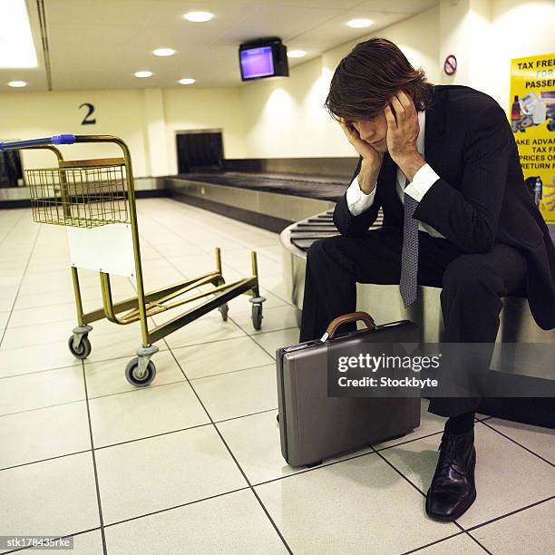 a young man sitting on a luggage conveyor belt and waiting for his luggage - belt stockfoto's en -beelden