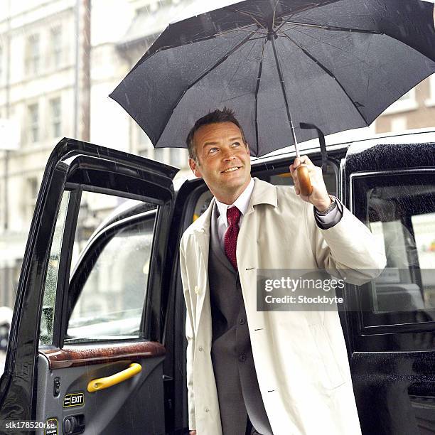 a man stepping out of a taxi with an umbrella - open roads world premiere of mothers day arrivals stockfoto's en -beelden