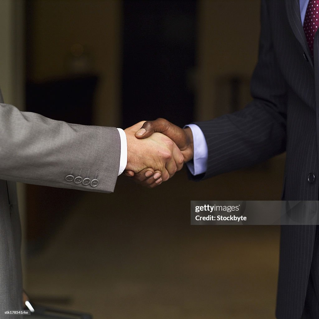 Close up mid section of two businessmen shaking hands