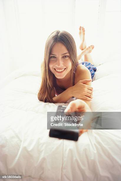 portrait of a young woman lying in bed operating a remote control - teen girl barefoot stock pictures, royalty-free photos & images