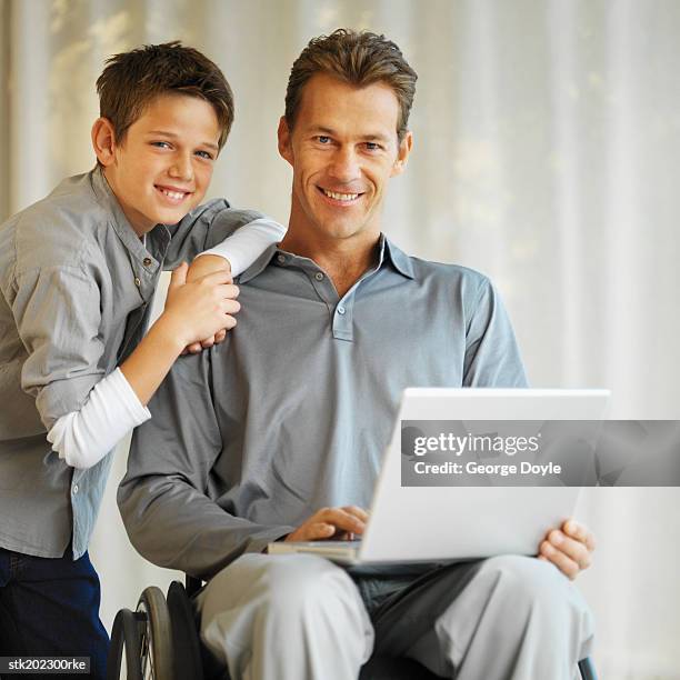 portrait of a man in a wheelchair showing his son (10-11) something on a laptop - menschliches gelenk stock-fotos und bilder