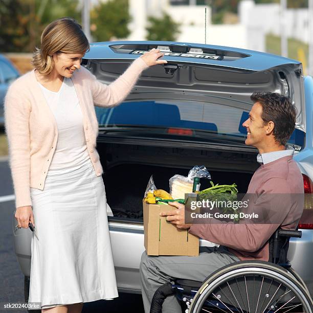 man sitting in wheelchair and wife bringing in groceries from car - closing car boot fotografías e imágenes de stock