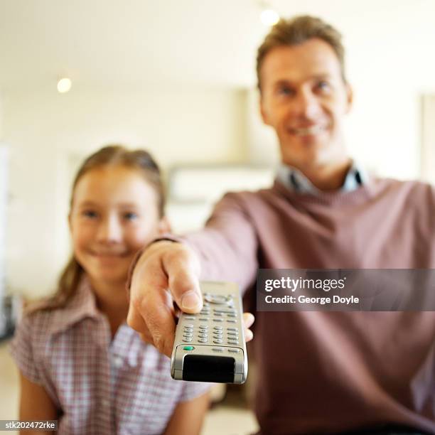 father and daughter (9-10) watching television and father holding remote control - control photos et images de collection