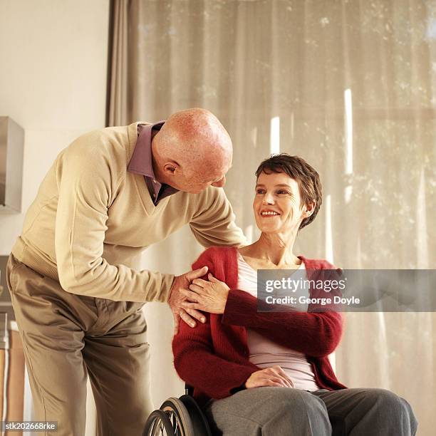 husband bending down to talk to wife who is sitting in a wheelchair - is stock pictures, royalty-free photos & images